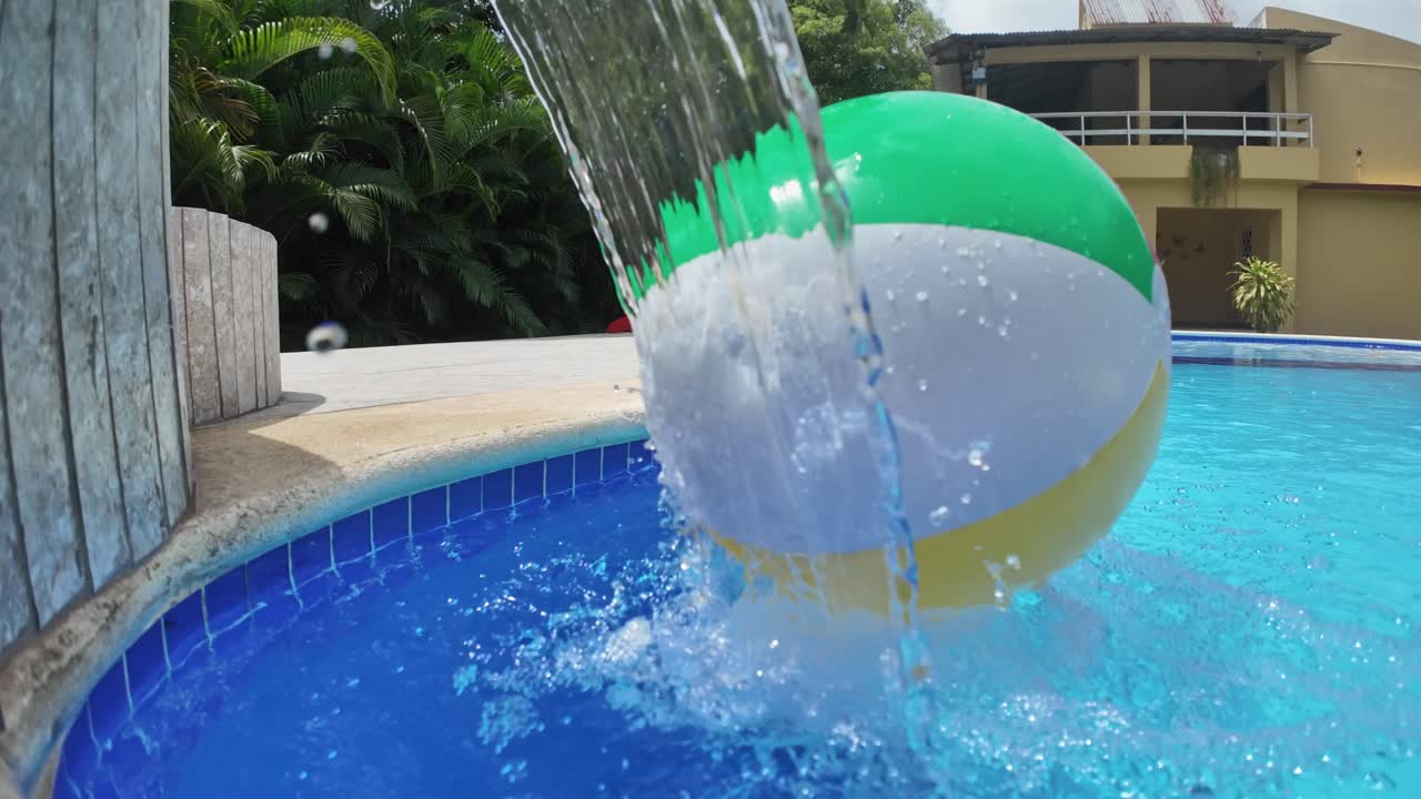Colorful and big inflatable ball rolling under pool water fountain. Static view
