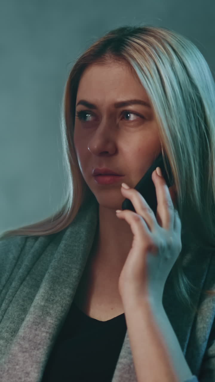 Confused blonde woman doctor examines x-ray picture talking on cellphone with patient sitting at table with bright lamp in hospital office in evening closeup slow motion