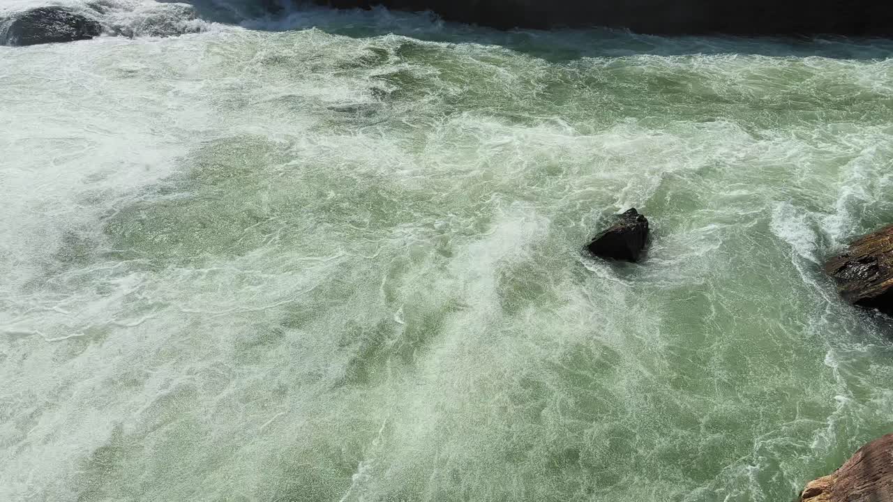 Nærbillede af kraftige flodstrømfald, der suser rundt om mørke klipper med hvirvlende strømme og skummende vand, der indfanger kraften og bevægelsen fra den hurtigt strømmende flod.