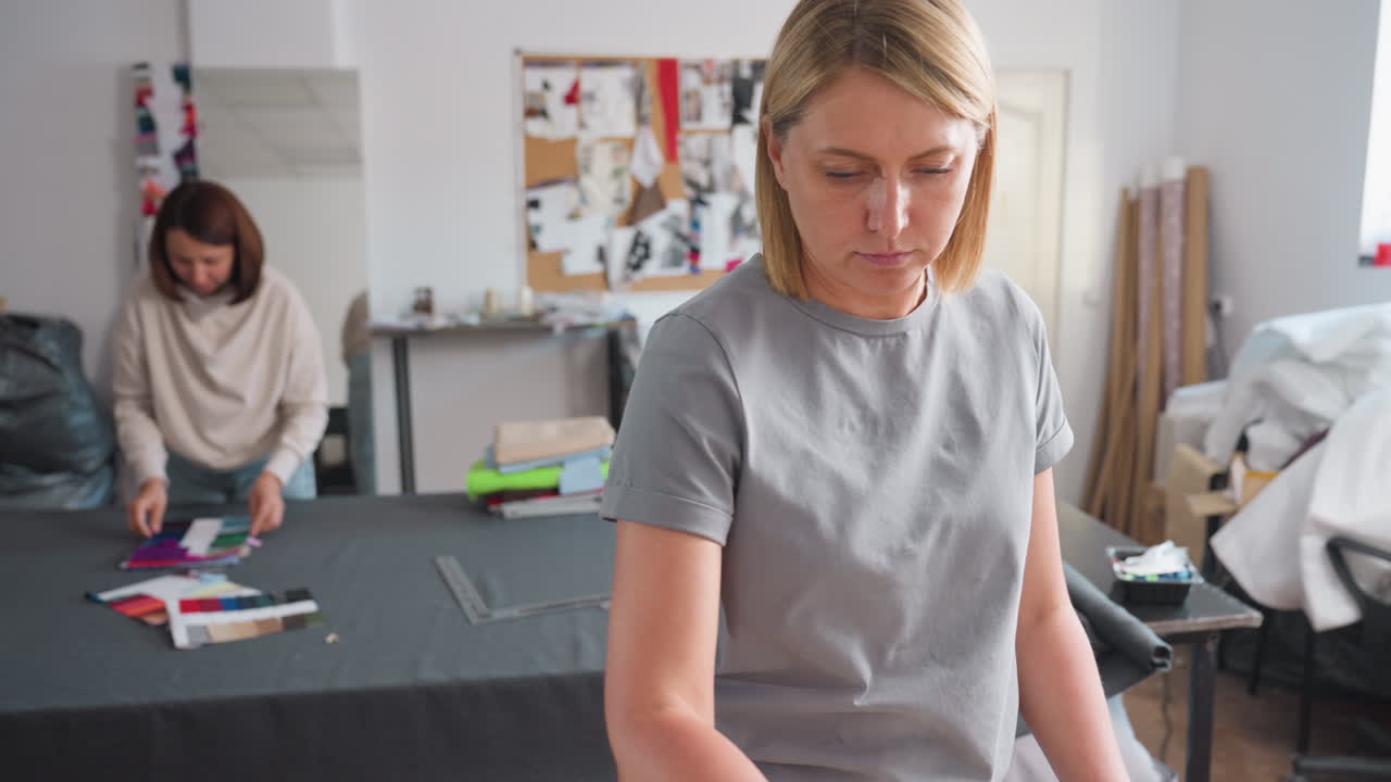 Fashion designers as one ironing and other arranging color pallets, focusing on synergy, refining garment details, ensuring cohesive style, demonstrating professional finishing, fostering creativity