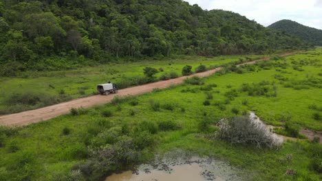 camión moviéndose en un camino de tierra húmeda en el paisaje rural de américa del sur a lo largo de la selva y las marismas, disparo de drones