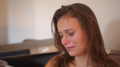 A-close-up-portrait-shot-of-a-young-woman-with-wounds-and-bruises,-stares-with-a-blank-look-and-starts-crying-while-touching-her-sore-cheek