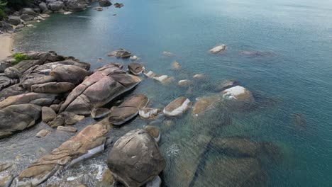 flying along a rocky beach with huge rocks with clear see through sea water