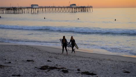 two surfer girls walking on the beach just after sundown