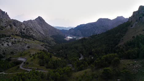 mountain massif in valley with winding roads and forests, drone aerial shot