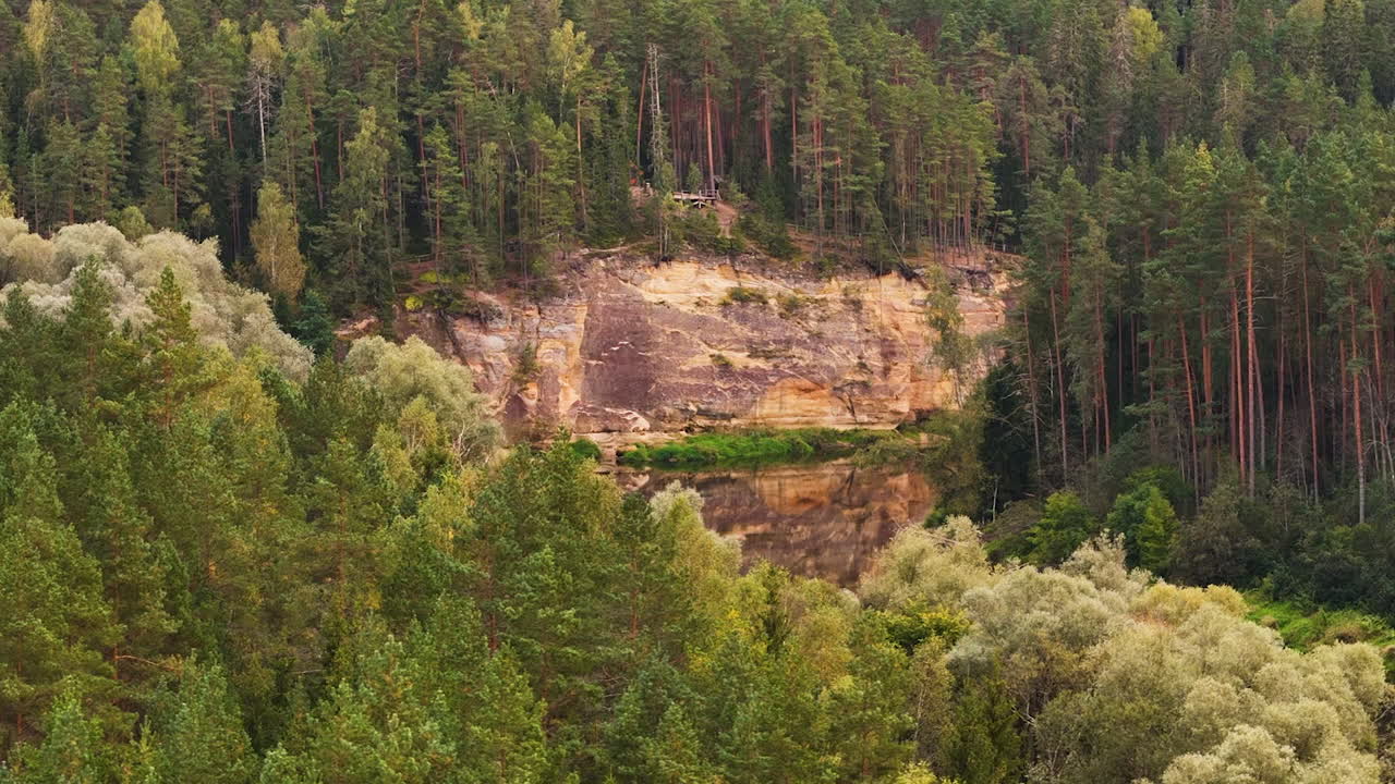Drone footage of sandstone cliffs in Latvia’s Gauja National Park, bordered by green forest.