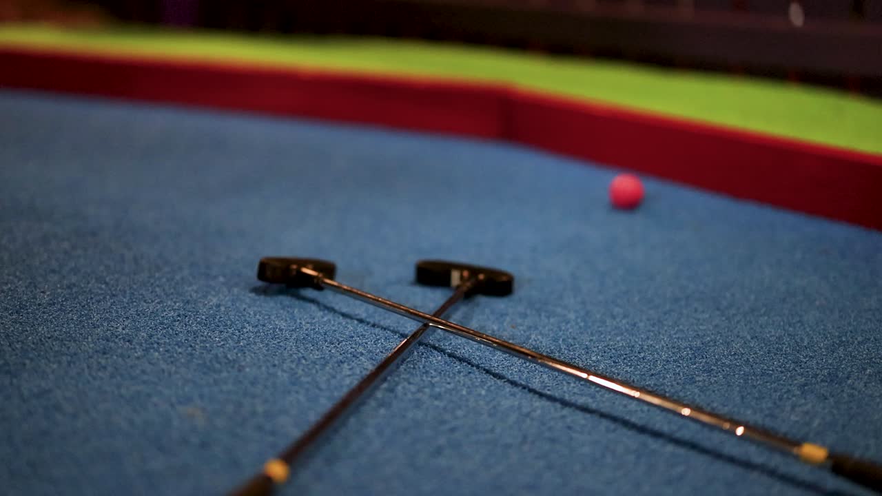 A golf ball bounces over two putters on a mini-golf course, captured in low-light conditions