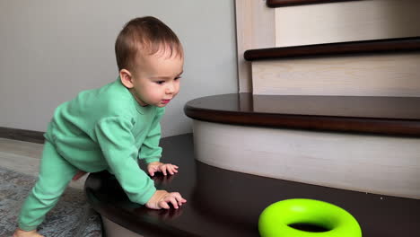 baby crawling on stairs and playing with a green toy ring