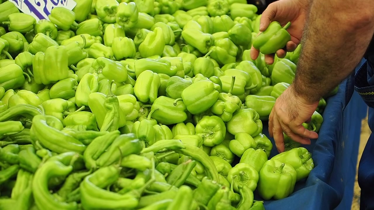 Cliente che seleziona peperoni verdi freschi al mercato.