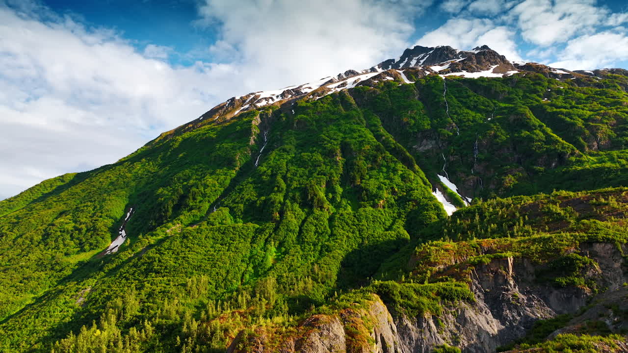 Green mountain slopes with summer snow. Bright green Alaskan slopes are streaked with thin summer snowfields under blue sky