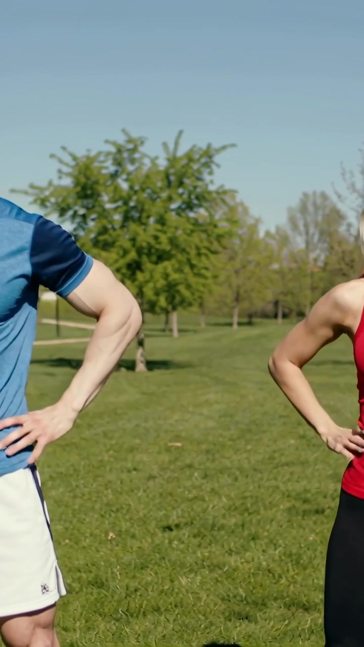 Vertical video: Couple doing fitness warmup on grass, beginning arms-up, lowering to hands on hips