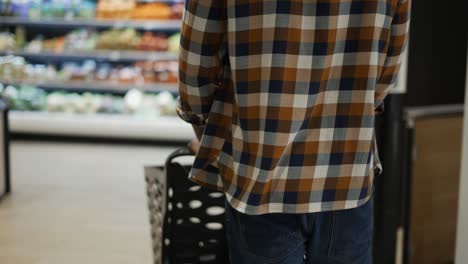 man pushing trolley along supermarket grocery aisle, rear view