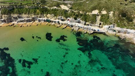 Disfrute-De-La-Serenidad-Aérea-De-La-Costa-De-La-Bahía-De-Gnejna,-Una-Instantánea-Pacífica-De-La-Armonía-De-La-Naturaleza-Y-La-Vida-Tradicional-Maltesa