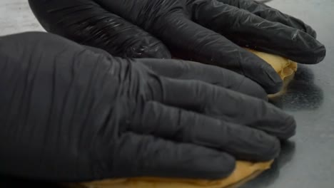 hamburger bun is placed on a restaurant grill by the gloved hands of a chef