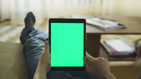 el hombre está acostado en el sofá en casa y usando la tableta con pantalla verde en modo paisaje