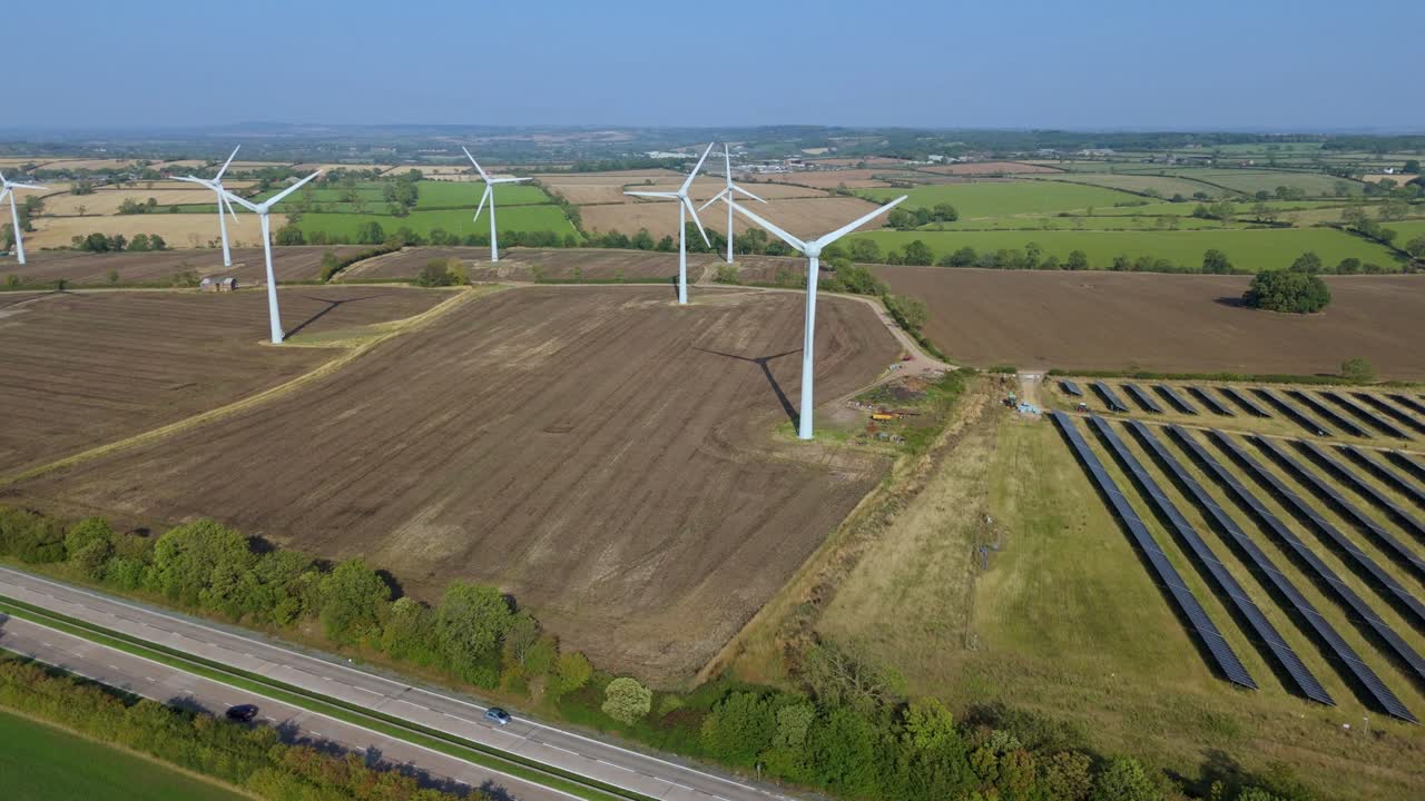 Aerial drone shot of large wind turbine and solar power plant generating renewable clean energy on sunny day near Loughborough England UK