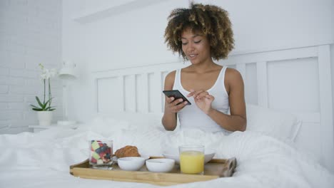 Mujer-Con-Teléfono-Inteligente-En-La-Cama-Con-Comida