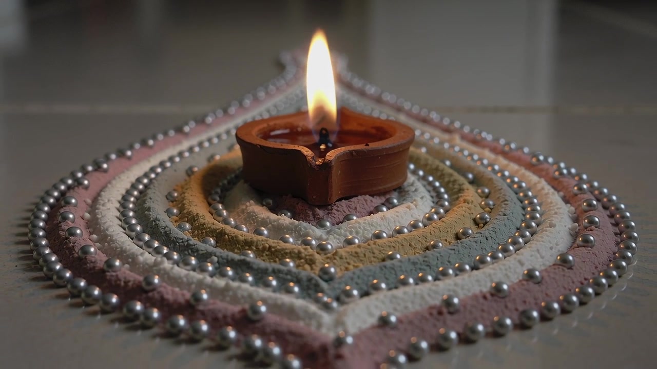 Flickering clay oil lamp showing oil shining on teardrop rangoli on tiled surface, camera widening