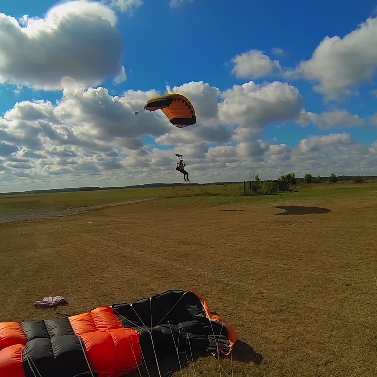 Parachutist slowly descending in the sky and landing softly. Beautiful blue sky with white clouds at backdrop