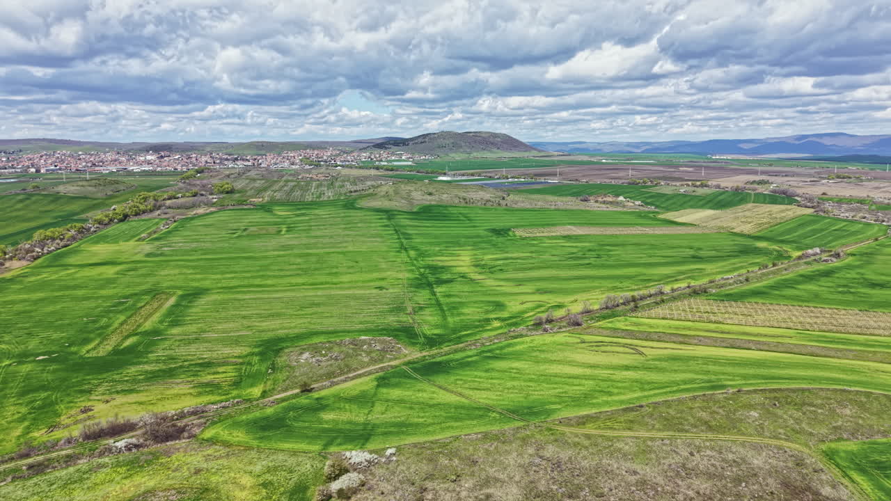 Campi verdi si estendono nel paesaggio con una città in lontananza sotto un cielo nuvoloso di giorno.
