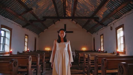 young woman standing in a simple church with lit candles, experiencing a moment of devotion and tranquility under a metal roof and wooden cross