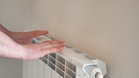 el hombre se calienta las manos con un radiador de calefacción