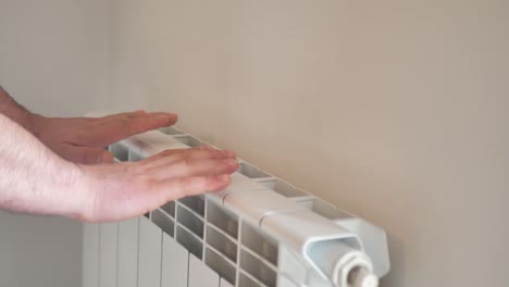 man warms his hands from a heating radiator