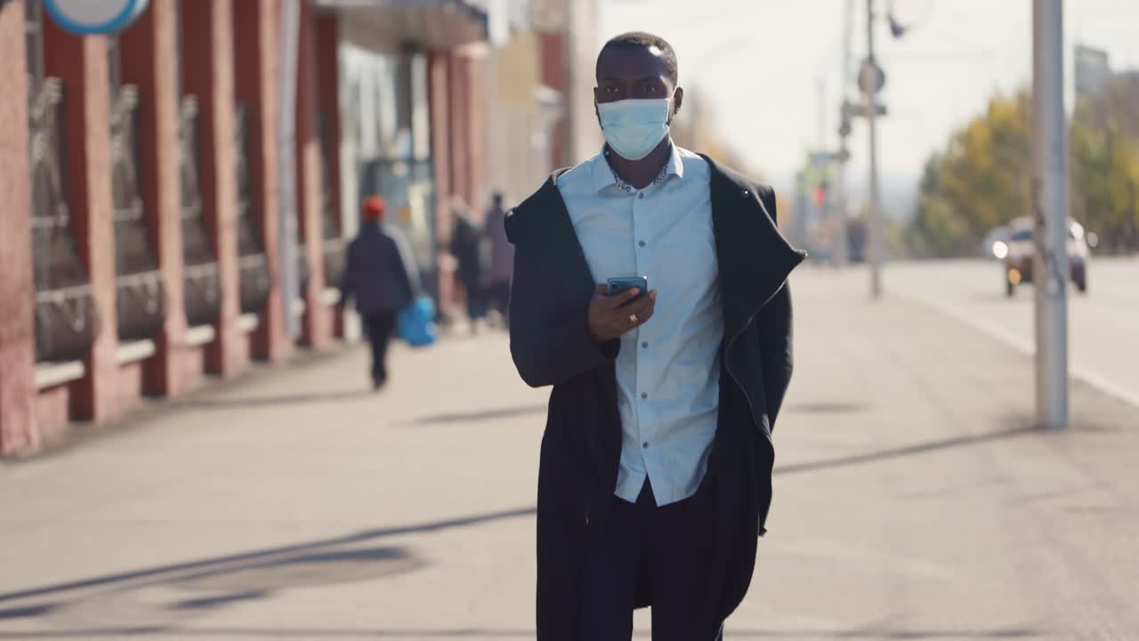 Man Wearing a Mask and Walking Down a City Street
