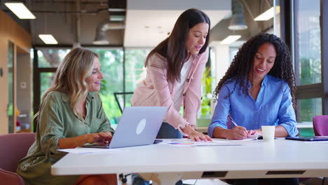 equipo de negocios femenino multicultural sentado en un escritorio con una computadora portátil en la oficina colaborando en un proyecto