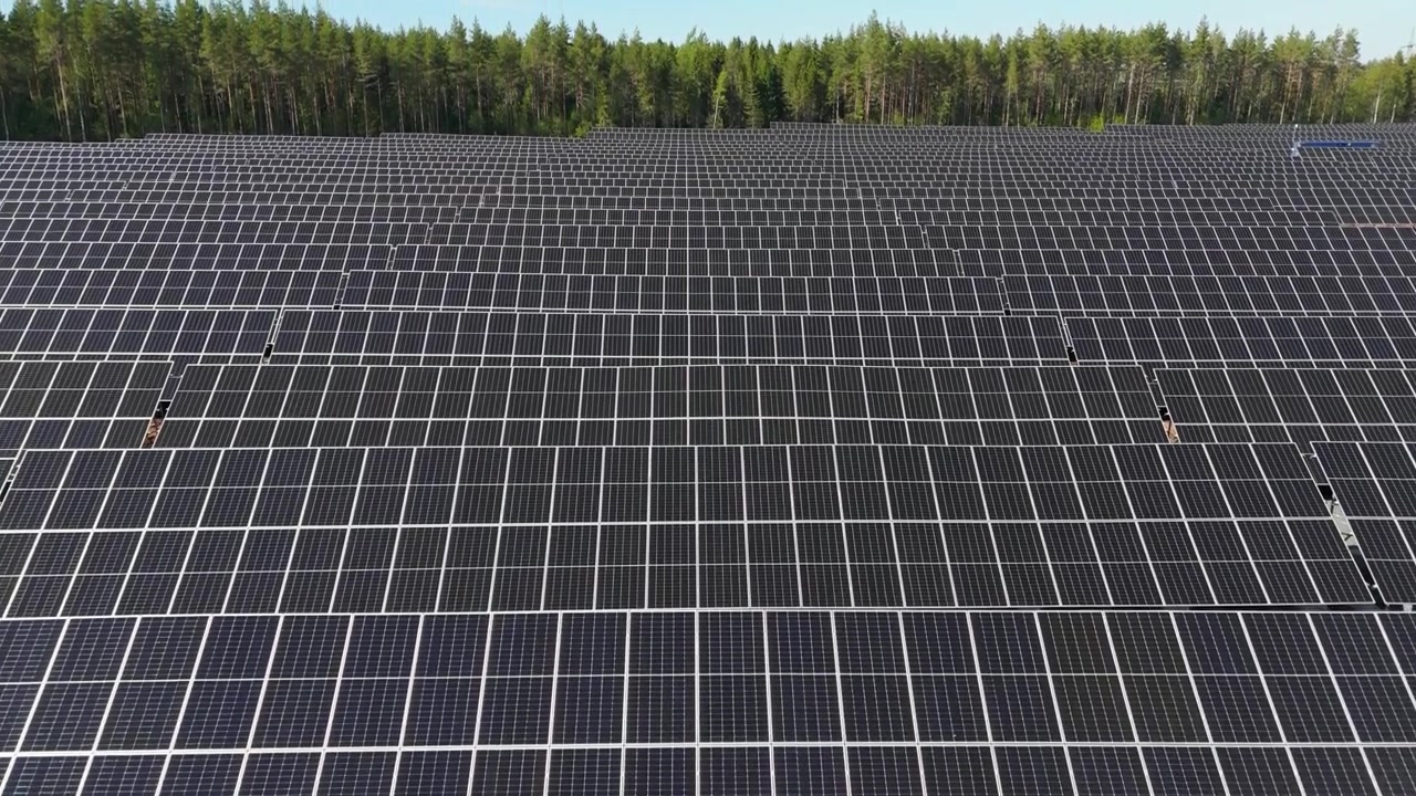 Panoramica aerea su una fattoria solare che mostra pannelli bifacciali che producono energia rinnovabile in Finlandia, file perfette e strutturate in una splendida colonna fino alla linea degli alberi, con un motivo a griglia industriale.
