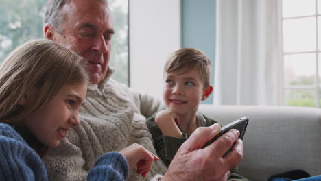 Abuelo-Jugando-Videojuegos-Con-Nietos-En-El-Teléfono-Móvil-En-Casa