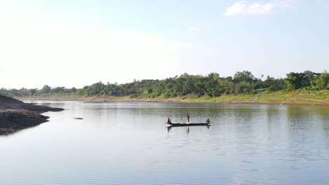 Aerial-shot-of-a-small-wooden-boat-with-fishermen-catching-fish-using-net-in-traditional-style-in-Surma-river,-Bangladesh