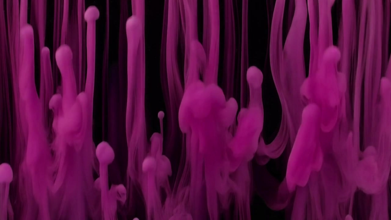 Gouttelettes d'encre rose s'élevant dans l'eau sur fond noir