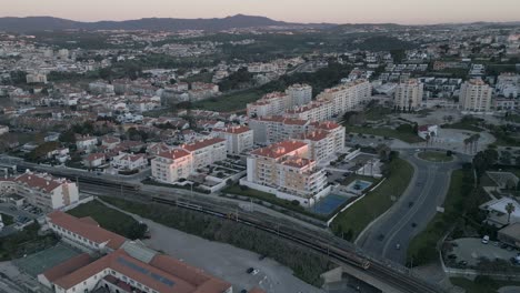 Imágenes-Aéreas-De-São-Pedro-Do-Estoril-Con-Trenes-En-Movimiento,-Cascais,-Portugal-Al-Amanecer