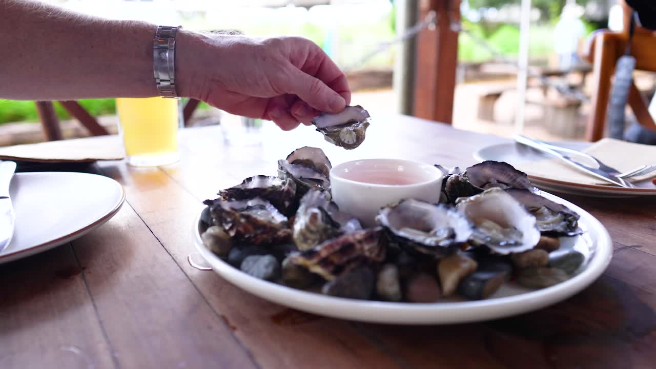 A hand reaches for oysters on a wooden table in natural light, capturing a relaxed dining moment in Byron Bay