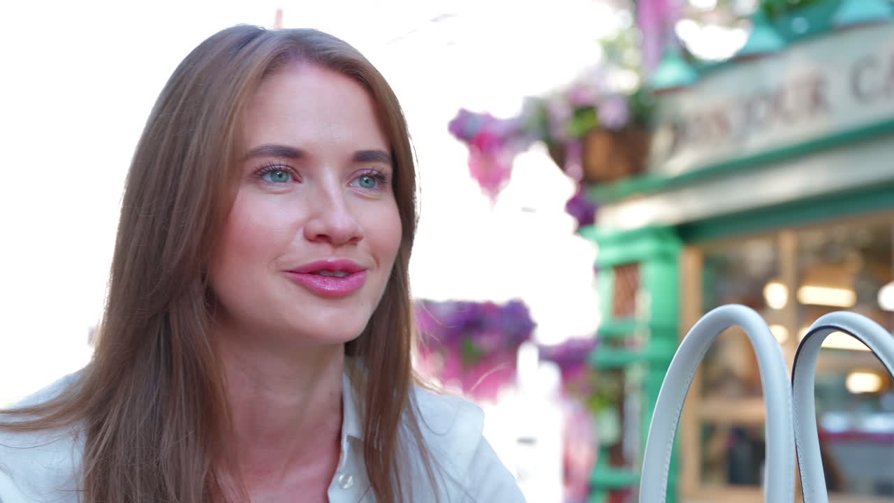 Brunette woman talking at a table with flowers on it, at an outdoor cafe