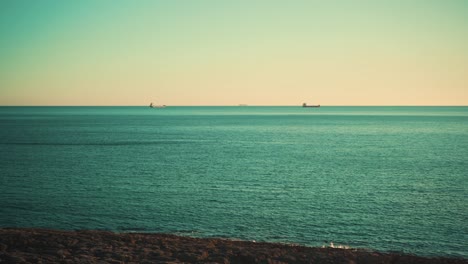 Rocas-Del-Acantilado-De-La-Costa-Del-Océano-Con-Barcos-De-Carga-Al-Atardecer-Con-Cielo-Azul-4k