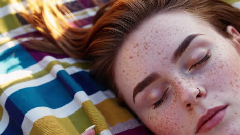 woman with freckles resting on a striped blanket in sunlight