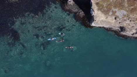 above kayakers in blue clear iceland water near rocky shore in fjord, aerial