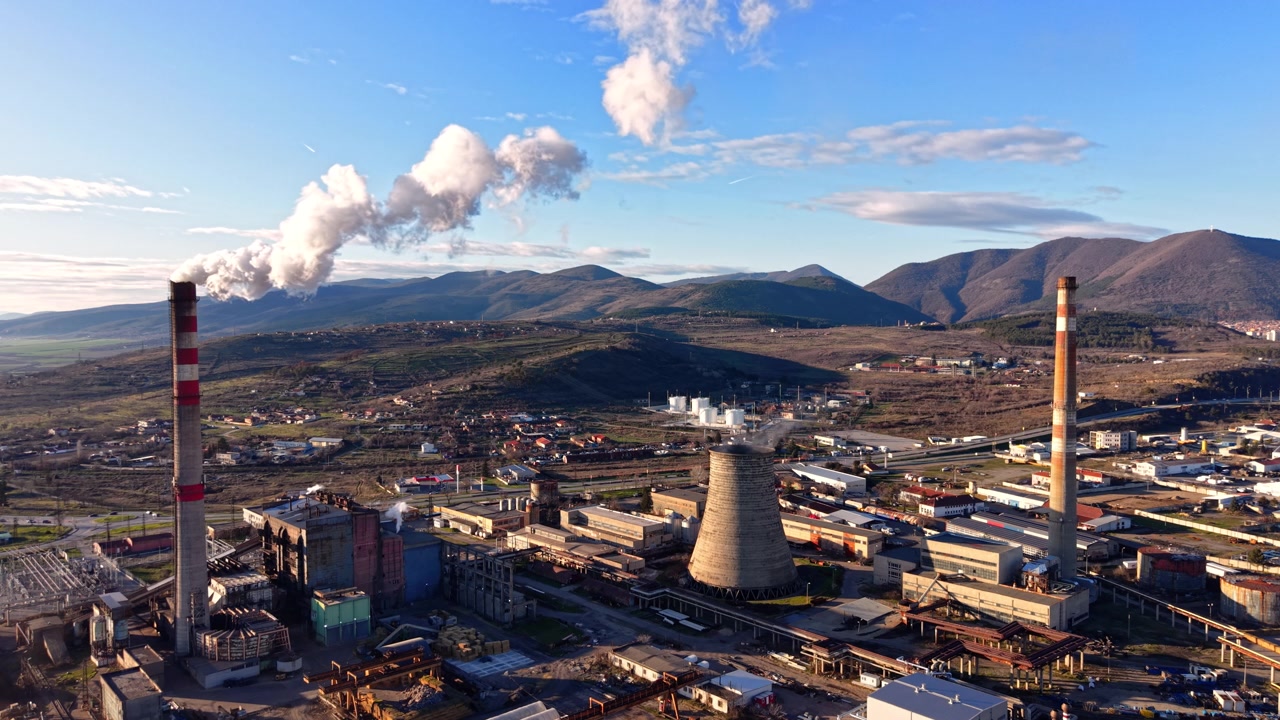 Torre de resfriamento industrial e chaminé com vapor. Fumaça branca flutua sobre um local de fábrica emoldurado por montanhas e telhados