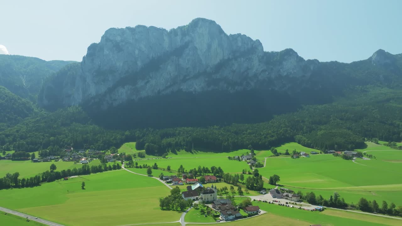 Drone cinematografico si libra all'indietro sopra una scenografica area rurale, svelando la famosa montagna Drachenwand vicino a Mondsee, Austria