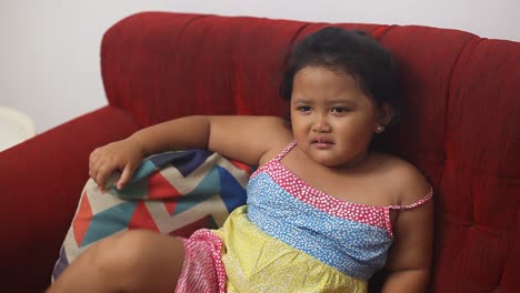 cute asian little girl sulking while siiting on the sofa at home