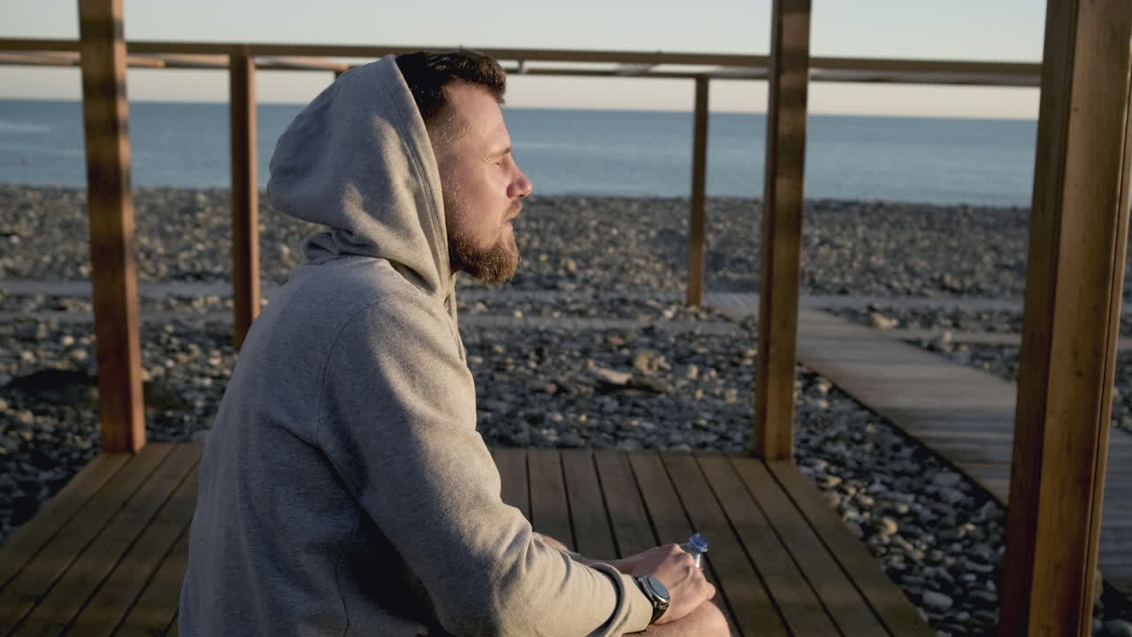 hombre bebiendo agua en la playa al atardecer