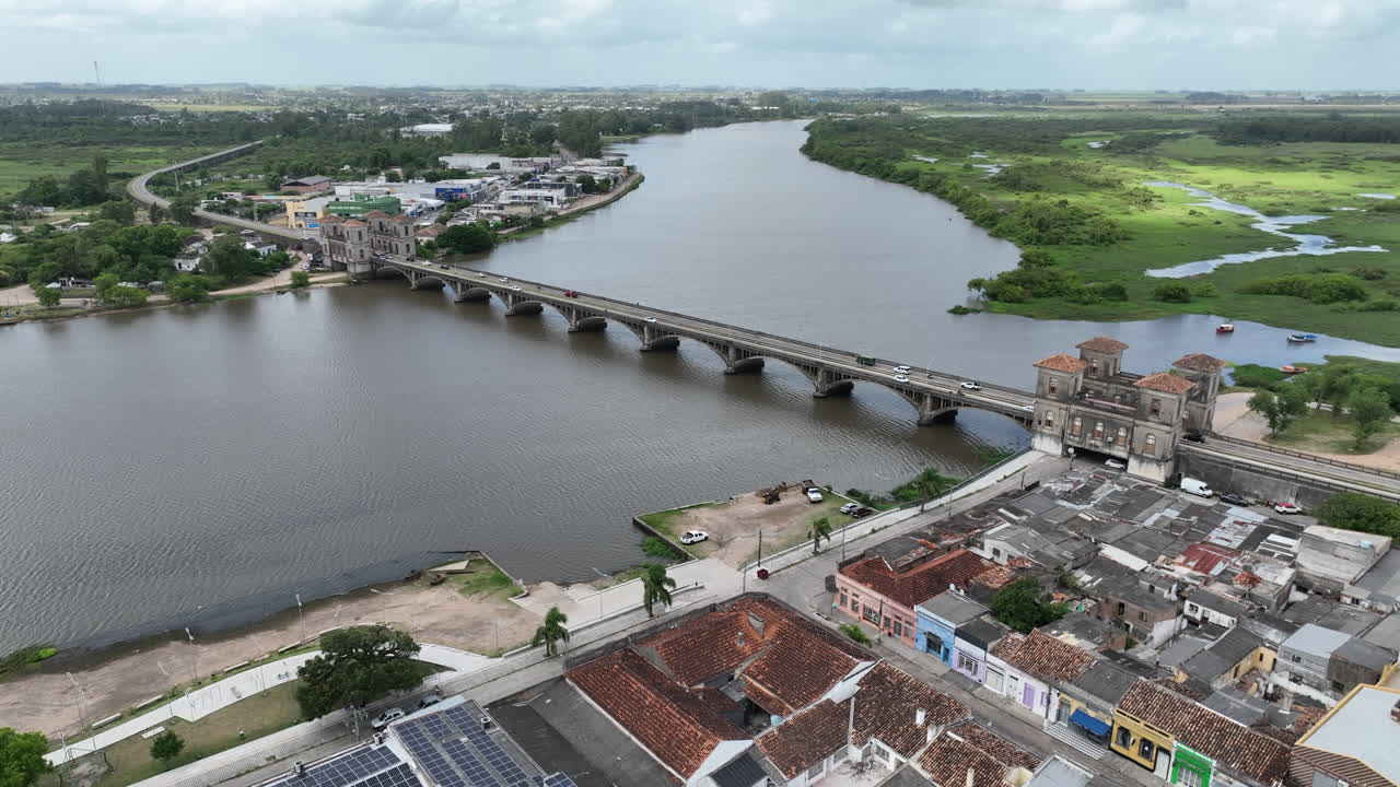 Afastamento e elevação cinematográficos revelando a histórica Ponte Internacional Mauá sobre o Rio Jaguaraão, que liga Jaguarão, no Brasil, a Rio Branco, no Uruguai, na fronteira internacional