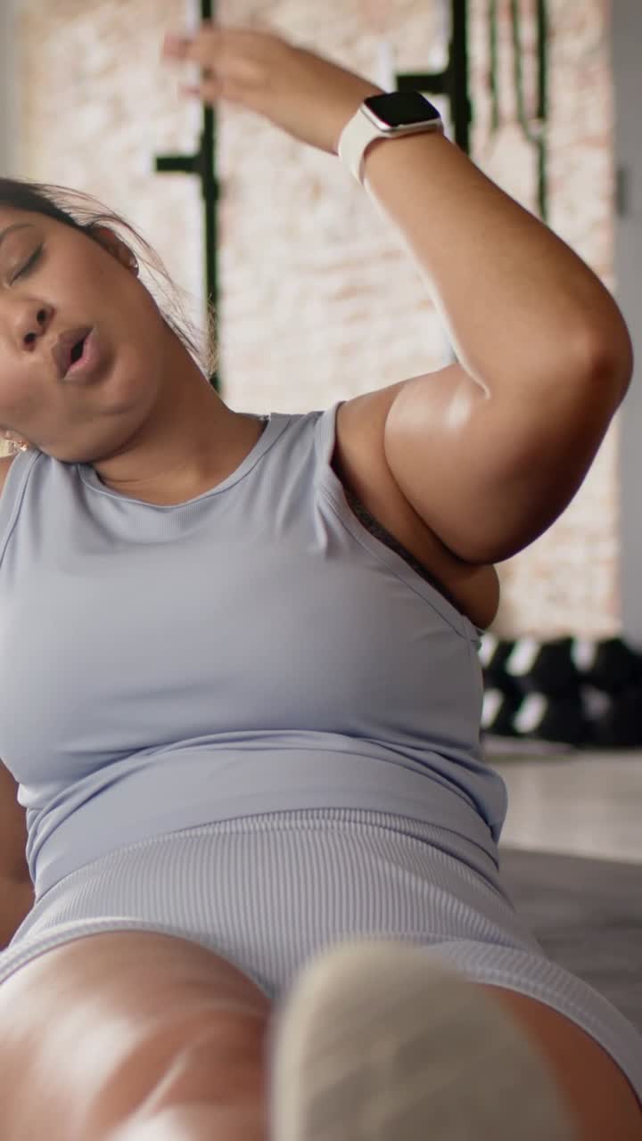 Video verticale: Donna in top grigio che inclina il braccio sinistro alzato, facendo esercizi di inclinazione laterale per gli addominali su un tappetino da palestra, con un orologio.