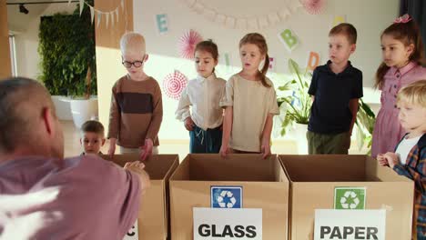 a man in a purple t-shirt is better than children how to properly dispose of garbage in a club to prepare children for school. the man teaches children how to properly sort their garbage