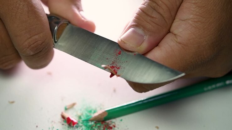 Footage of hands slowly sharpening a pencil and some coloured pencils with a sharp knife