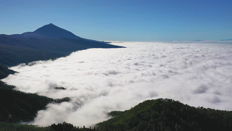 Aerial-shot-of-a-scenic-view-from-Pico-de-Teide-on-Canary-Islands-with-a-heavy-cloud-inversion-below-the-mountains-and-forests-and-a-clear-blue-sky-above