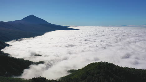 aerial shot of a scenic view from pico de teide on canary islands with a heavy cloud inversion below the mountains and forests and a clear blue sky above