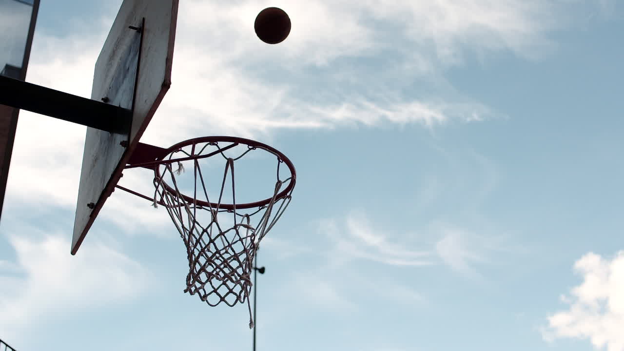 hombre metiendo una pelota de baloncesto afuera contra un cielo azul